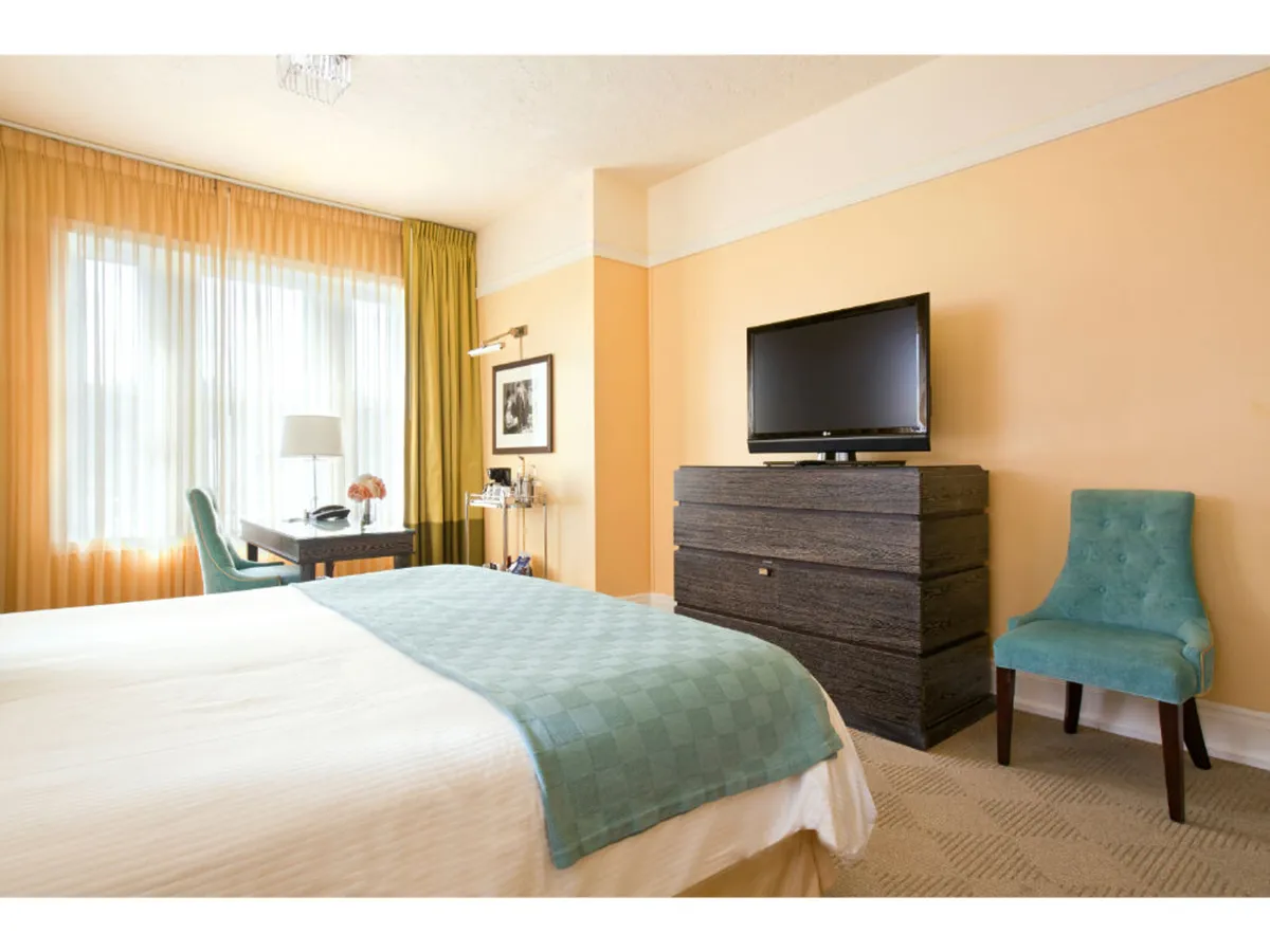 A thoughtfully arranged bedroom showing a generous king bed paired with a sleek desk and chair for efficient work. The television and soft curtains add to the room's serene ambiance, while the overall design balances both productivity and restful escape. The setting hints at enjoying morning coffee at the desk or relaxing with a late-night movie in bed.