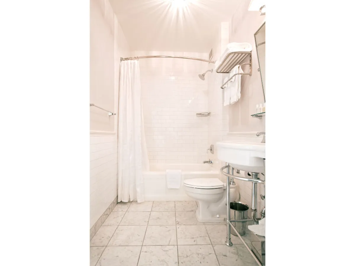 A serene bathroom scene featuring a clean bathtub/shower combination, a neatly arranged sink and countertop, a toilet, and a simple shower curtain. The space is uncluttered and well-lit, evoking a sense of calm and refreshment. Towels and subtle decor contribute to the atmosphere of cleanliness and comfort.