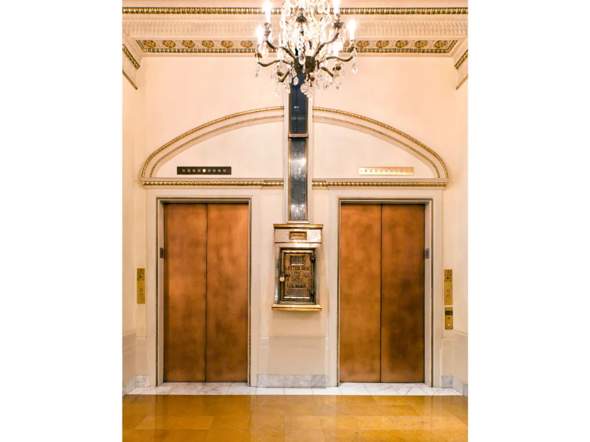 This image captures the hotel lobby, highlighting the elevators framed by decorative wall elements and an elegant chandelier overhead. The scene suggests a sense of arrival and anticipation, reinforced by the inviting yet luxurious atmosphere. While no pets are visible, the communal space is a transitional area where guests—potentially with pets—might pass through as they embark on city adventures or return from walks.