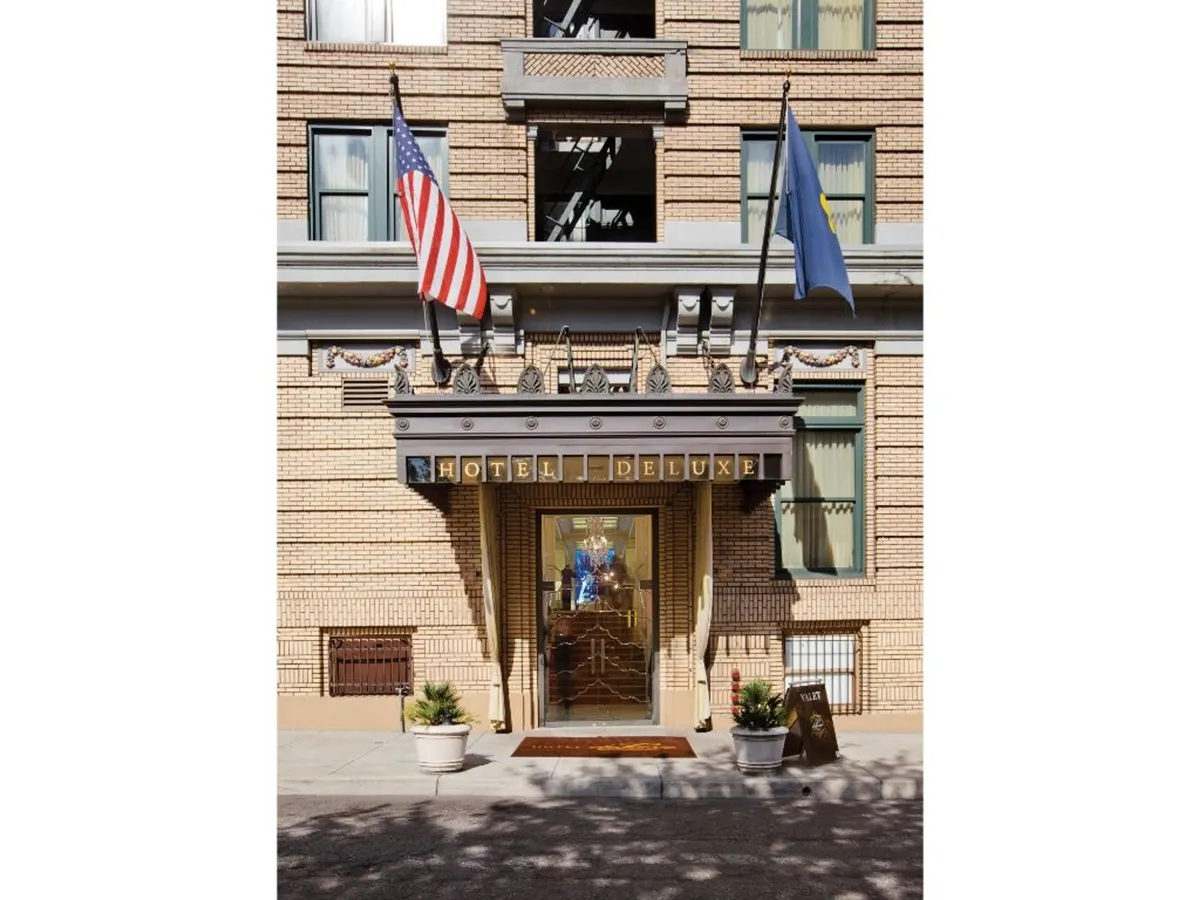 A welcoming exterior view shows the grand entrance to the historic hotel, complete with elegant flags and prominent signage. The hotel’s facade exudes timeless luxury, hinting at the plush amenities and storied ambiance awaiting inside. This shot sets the scene for arrival and exploration.