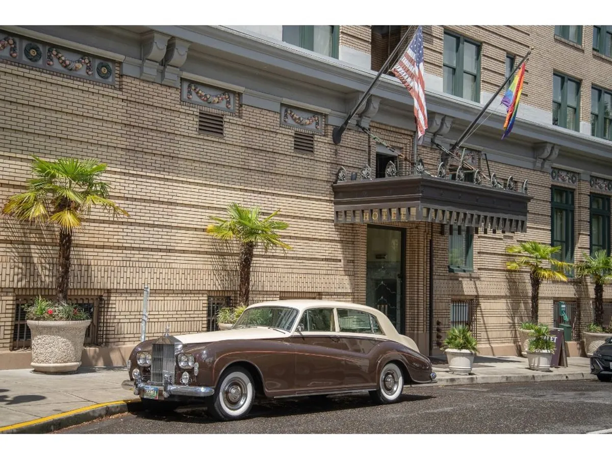 This exterior image presents a classic vintage car under the entrance awning, framed by palm trees and flags. The setting basks in sunlight, suggesting celebratory arrivals and special occasions. The scene’s elegance and nostalgia nod to the hotel's storied past and its romantic appeal for couples.