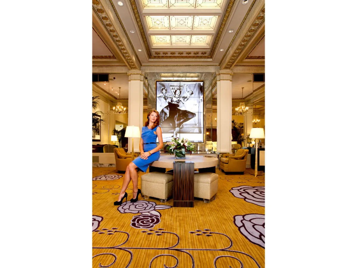 This image showcases a sophisticated lounge area with a woman in a blue dress, a stunning floral arrangement, and a decorative ceiling. The ambiance is social and welcoming, reflecting the comfort and luxury that guests—pets included—can expect. The presence of people socializing hints at the hotel’s vibrant yet relaxed atmosphere, where pets and owners alike can unwind after city explorations.