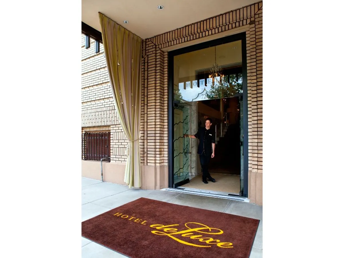 This exterior image showcases the hotel’s entrance, with the hotel logo visible on the mat and a staff member offering a warm welcome. The elegant doorway and stylish façade create an immediate sense of professionalism and hospitality, setting the tone for business travelers upon arrival.
