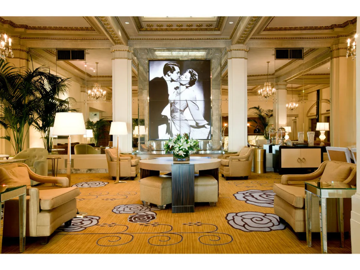 A vibrant event space featuring a striking black and white artwork as the focal point, a central circular table with a lush floral arrangement, and luxurious furnishings. The ambiance is both luxurious and welcoming, perfect for gatherings and celebrations.