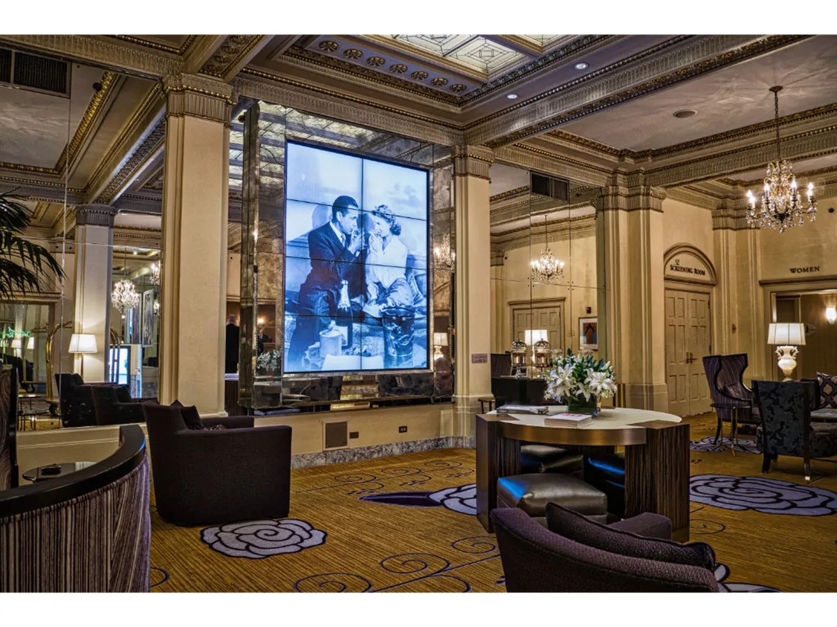 A sophisticated seating area within the hotel, highlighted by a large digital art display and ornate chandeliers. The space is designed for both art appreciation and social gatherings, providing an inviting setting for guests to network, relax, and enjoy curated visual art.