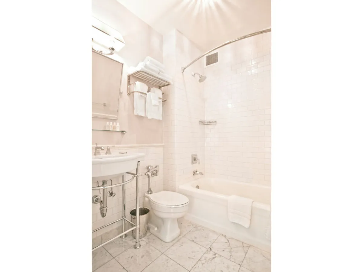 A bright, modern bathroom with a bathtub, a sink area, toilet, and plush white towels. The clean lines and soothing color palette create a tranquil environment, ideal for self-care routines or a relaxing soak. The space appears professionally maintained, reflecting high standards of cleanliness.